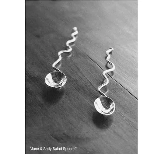 Two metal salad spoons with twisted handles placed on a wooden surface.