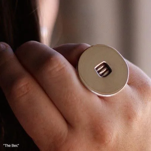 Close-up of a person's hand holding a silver key with a unique rectangular hole, part of a jewelry ring on their finger, with a blurred background.