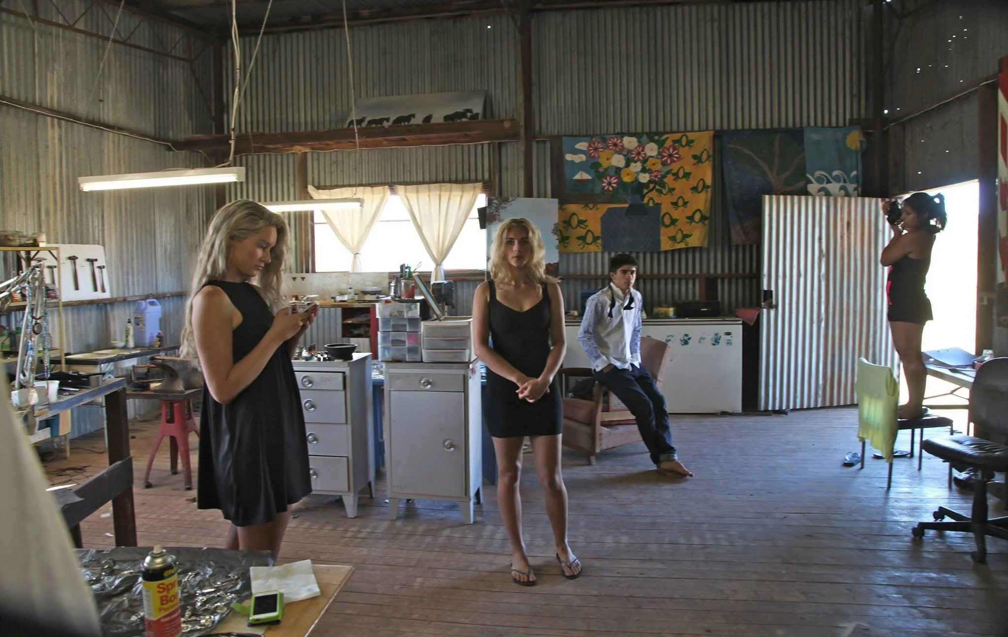 Indoor scene with four women in casual attire, various supplies, and artwork on the walls, in a rustic, metal-walled space with wooden floors.