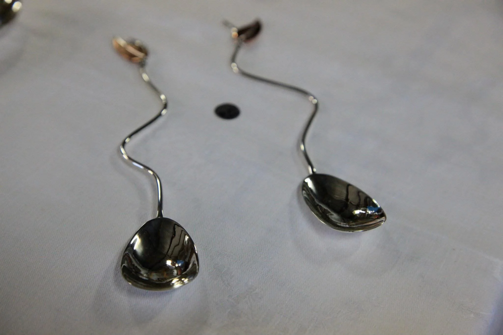 A close-up of five reflective silver spoons with curved handles, arranged on a white surface.