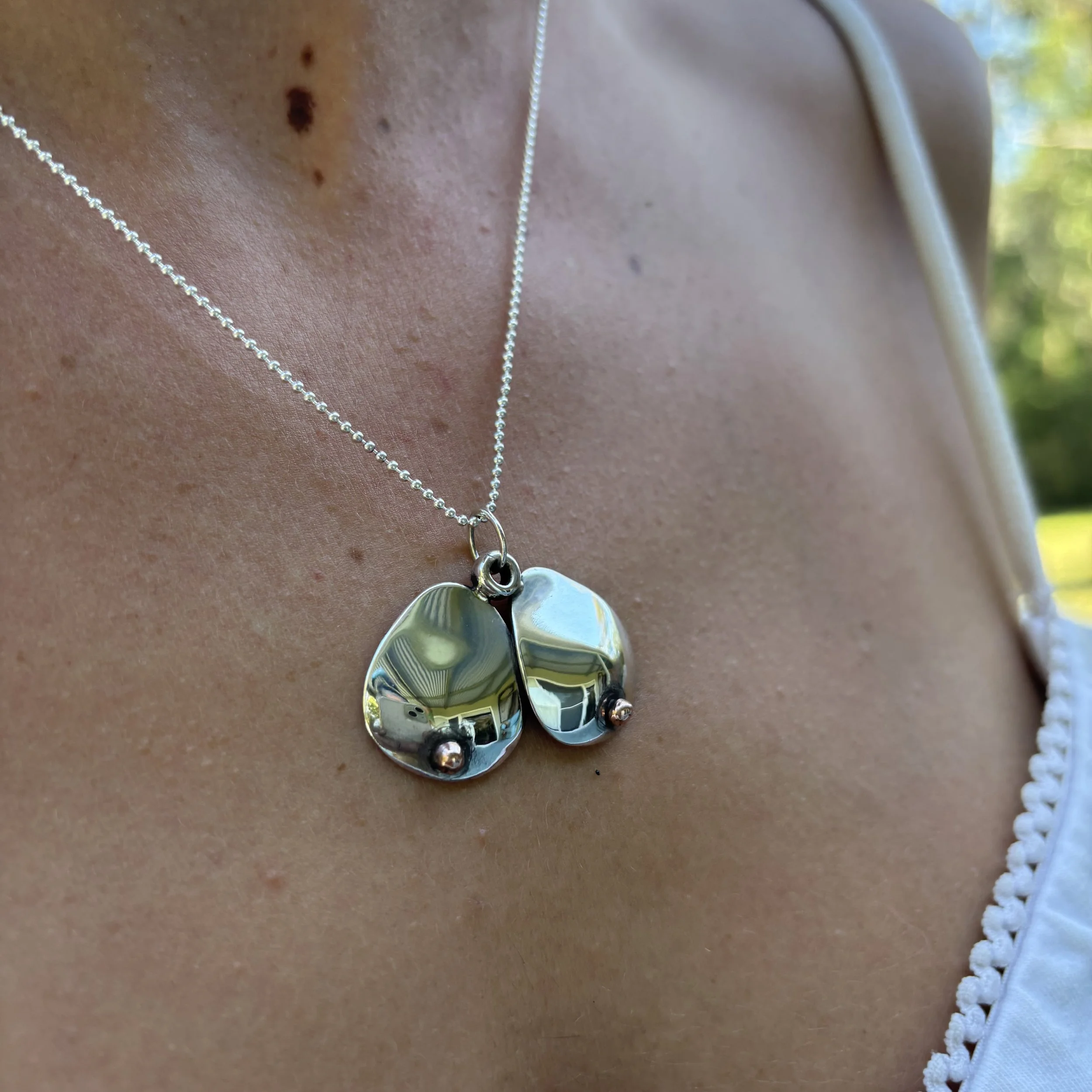 Close-up of necklaces with large metallic pendant on a person's neck, with dark freckles.