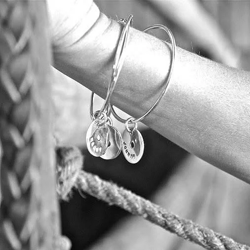 Close-up of a person's arm wearing jewelry, including a bracelet and two bangles with smiley face charms, resting on a rope.