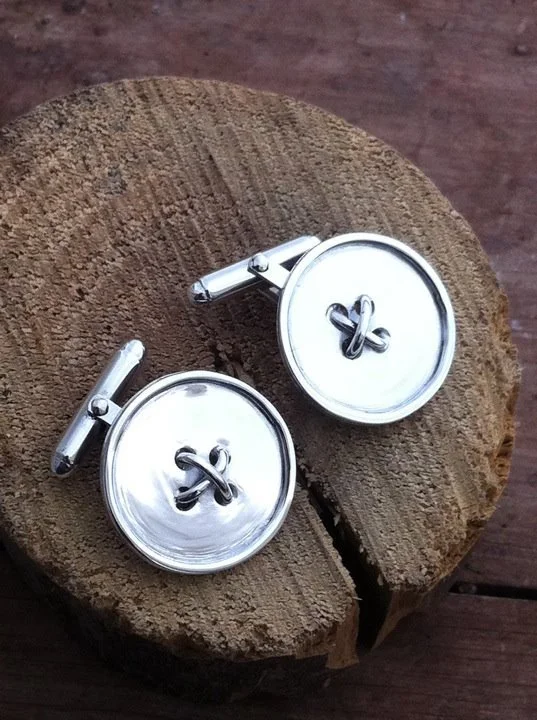 Silver round cufflinks with a black logo on a wooden surface.