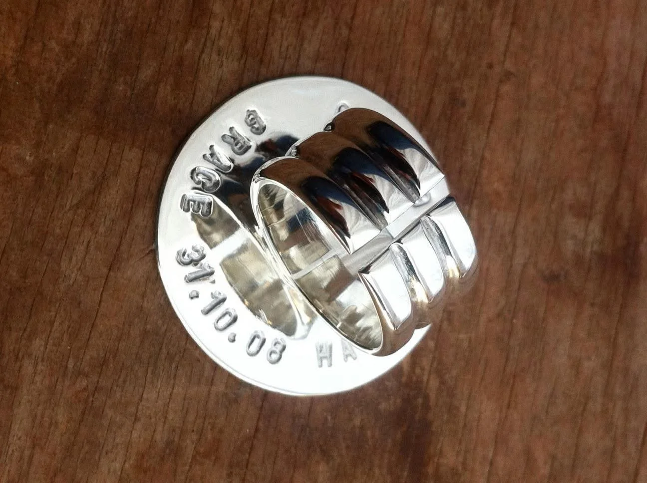 A shiny metallic doughnut-shaped cookie cutter with engraved text on the top, placed on a wooden surface.