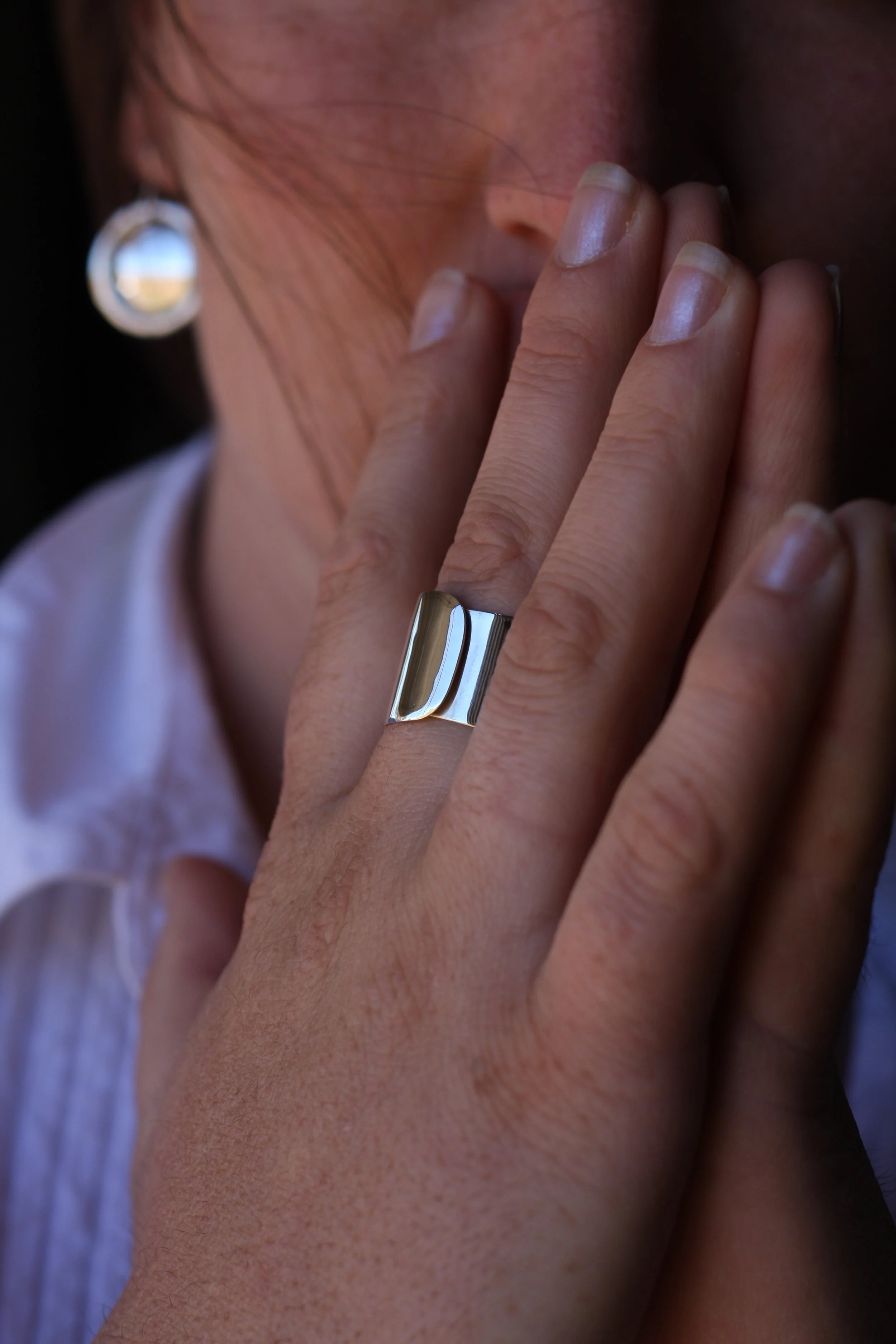Close-up of a person with a silver ring on their finger, touching their lips with their fingers, wearing an earring and a blazer with a striped shirt.