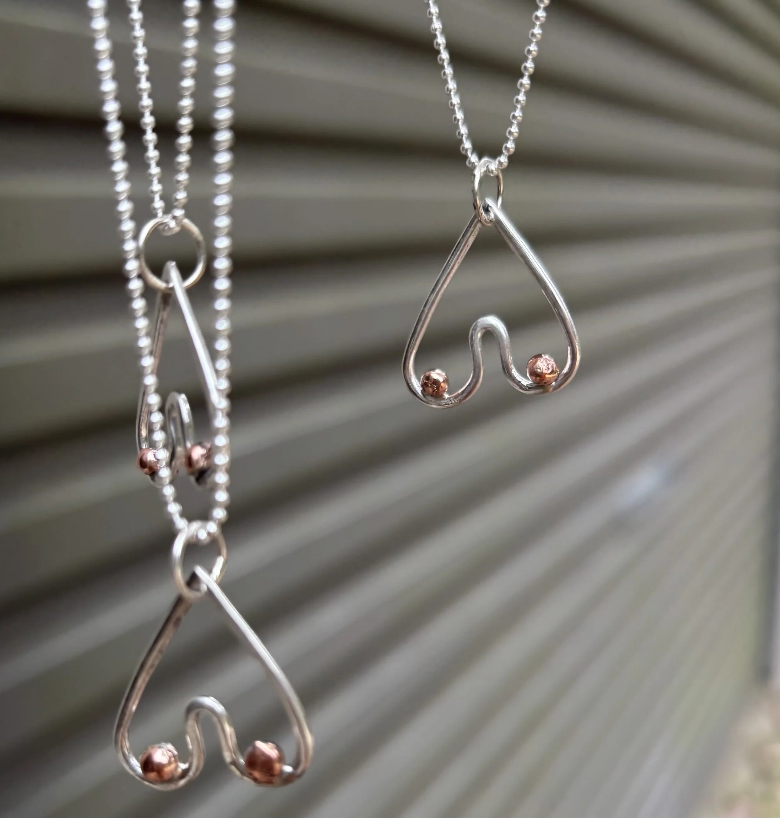 Close-up of silver and copper jewelry hanging on display with blurred horizontal lines in the background.