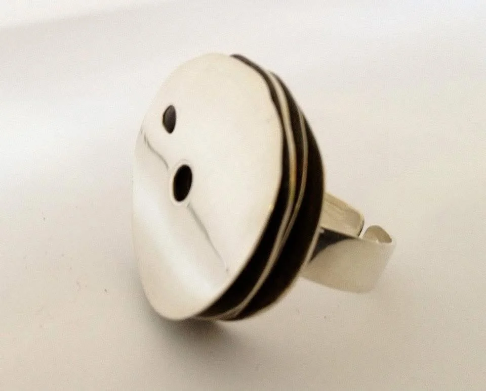 Close-up of a silver pin with a Darth Vader mask design, featuring two black oval eyes.
