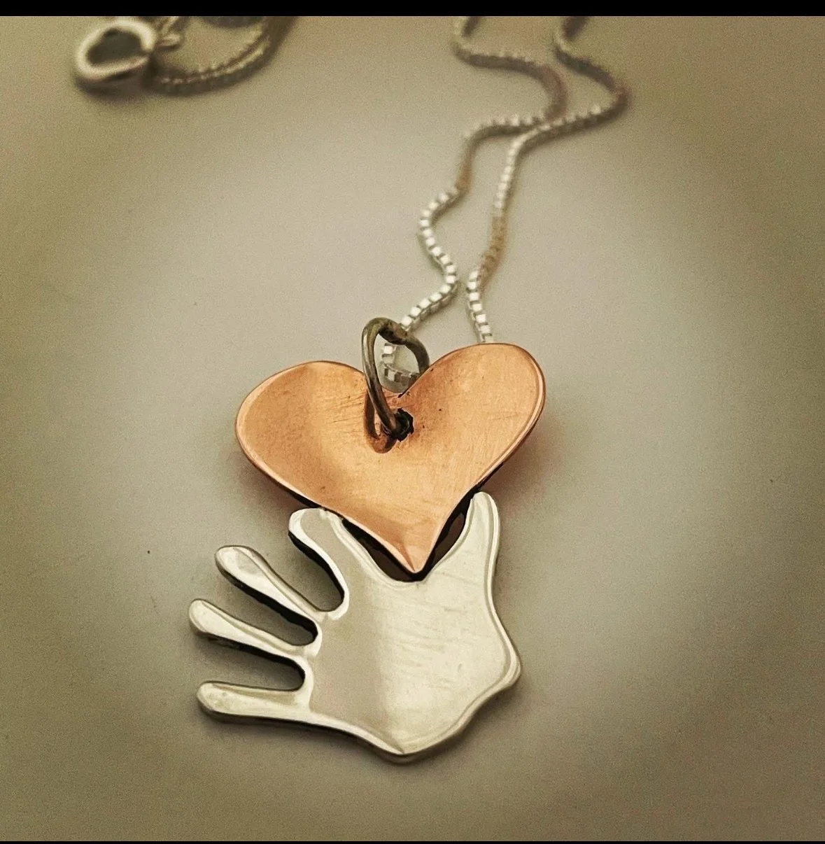 A necklace with a pendant featuring a white hand-shaped charm and a copper-colored heart-shaped charm attached to a silver chain.