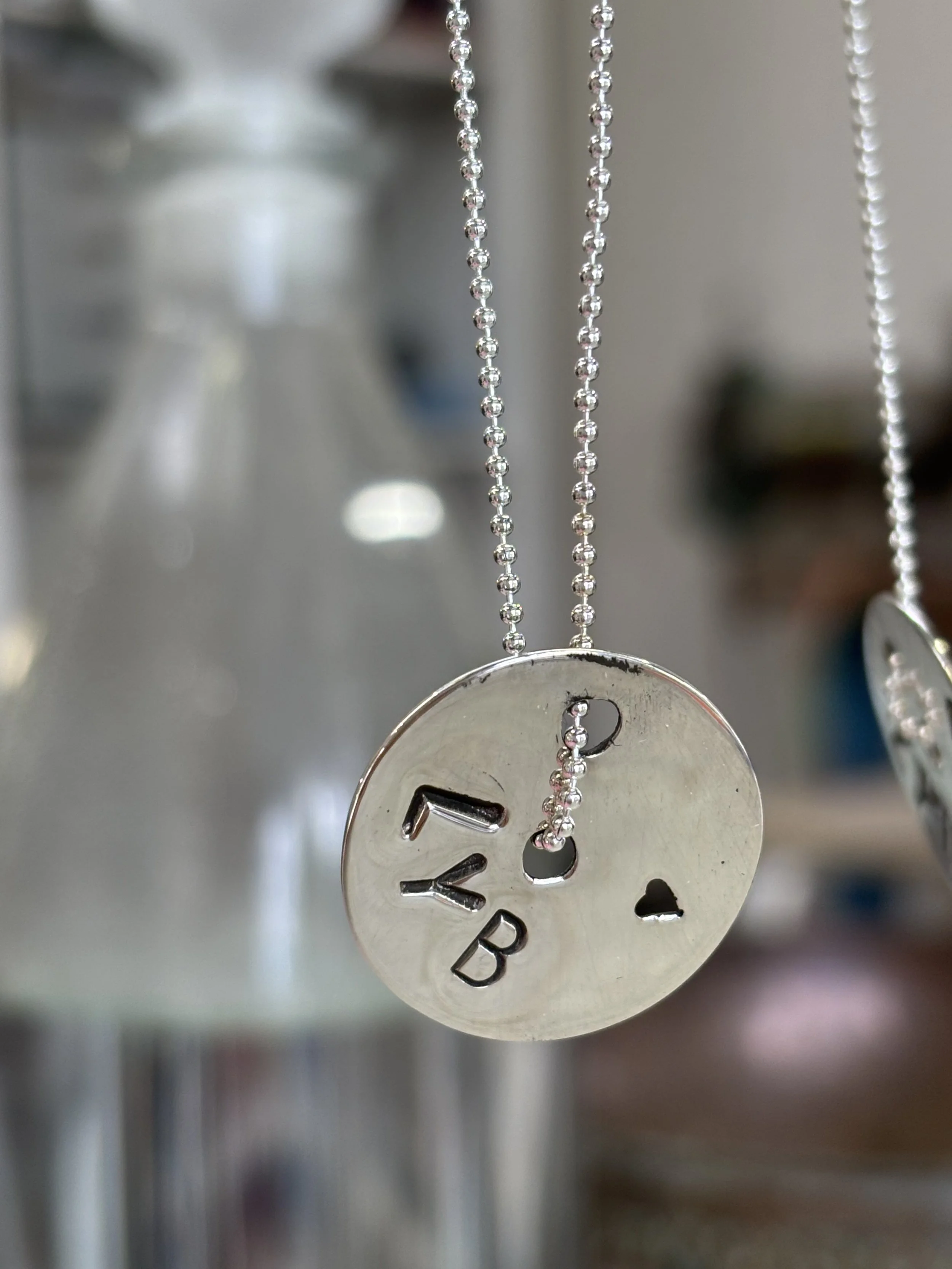 Close-up of silver metallic chain with a round pendant engraved with the word 'Baby' hanging from a necklace.