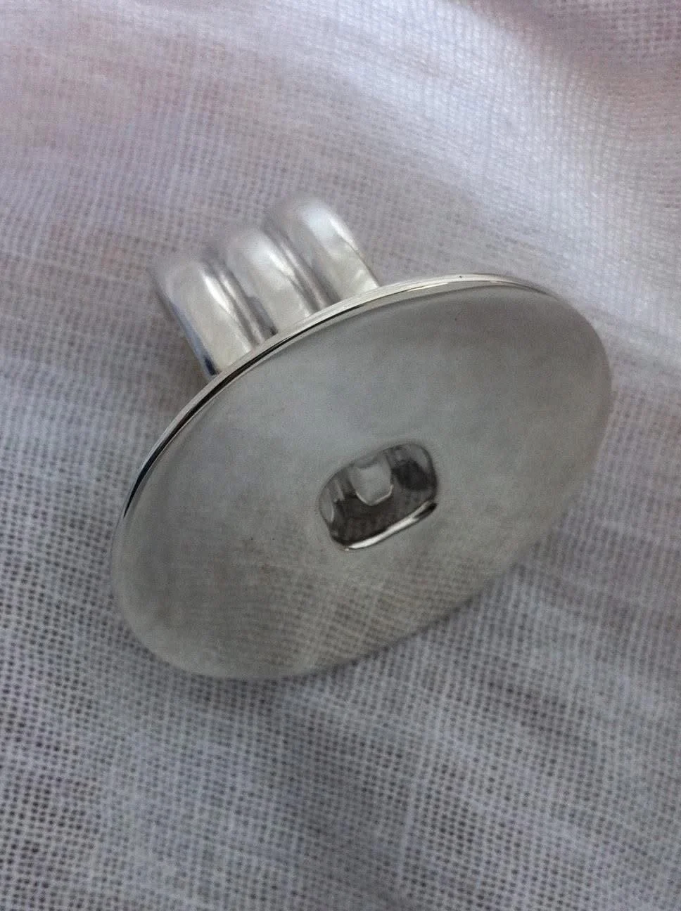 A silver, oval-shaped apple-shaped object with three protruding tubes on one side, resting on a textured white surface.