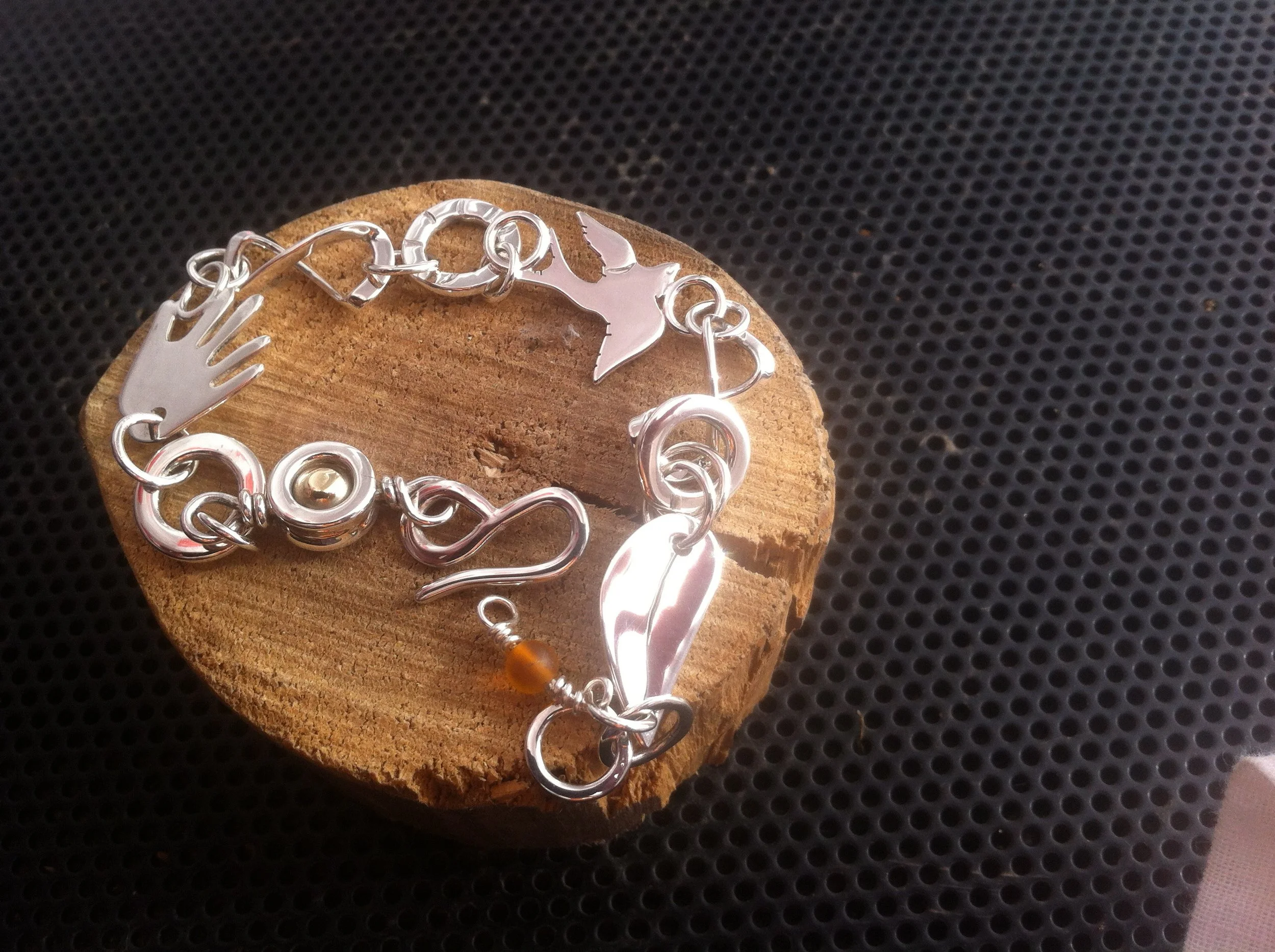 Silver jewelry bracelet with various charms, including a witch hat, for an adult or teen, displayed on a wooden surface.