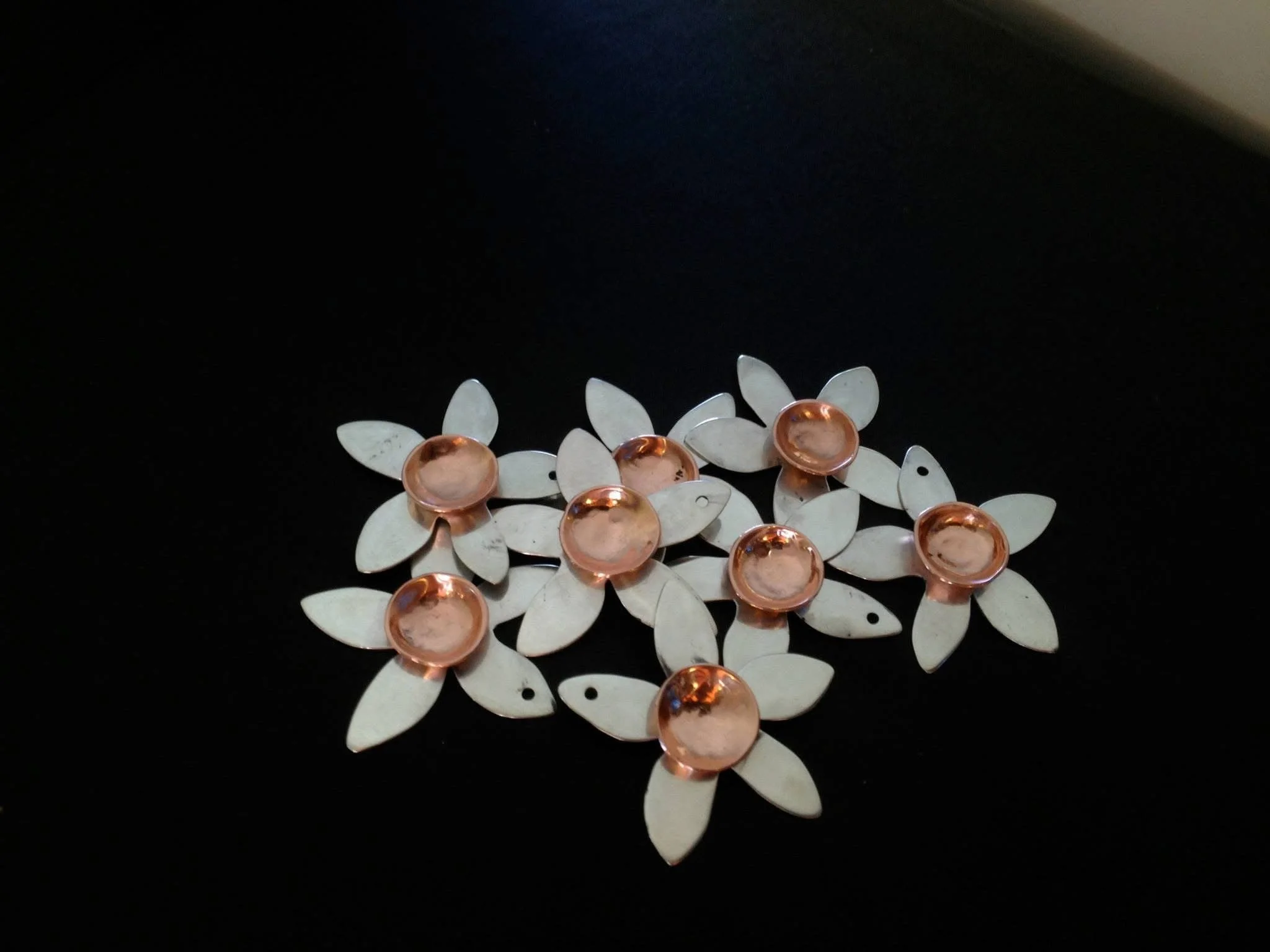 A piece of jewelry with cream-colored petal-shaped components and copper-colored circular accents on a black background.