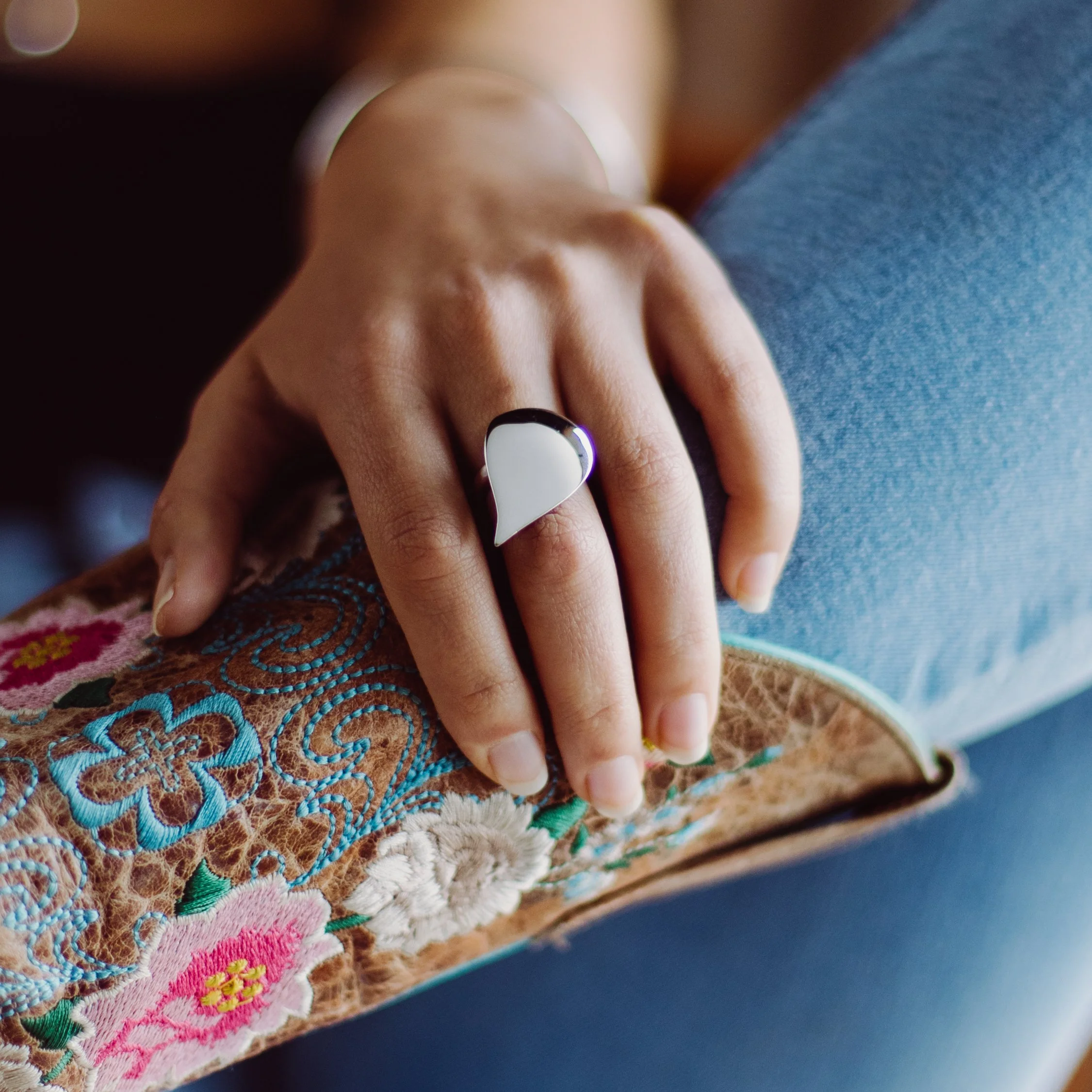 Close-up of a hand with nails painted black and white, resting on embroidered fabric with colorful floral designs.