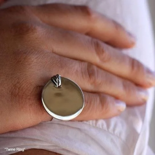 Close-up of a hand with a large, round, silver ring on the finger, resting on a white fabric surface.