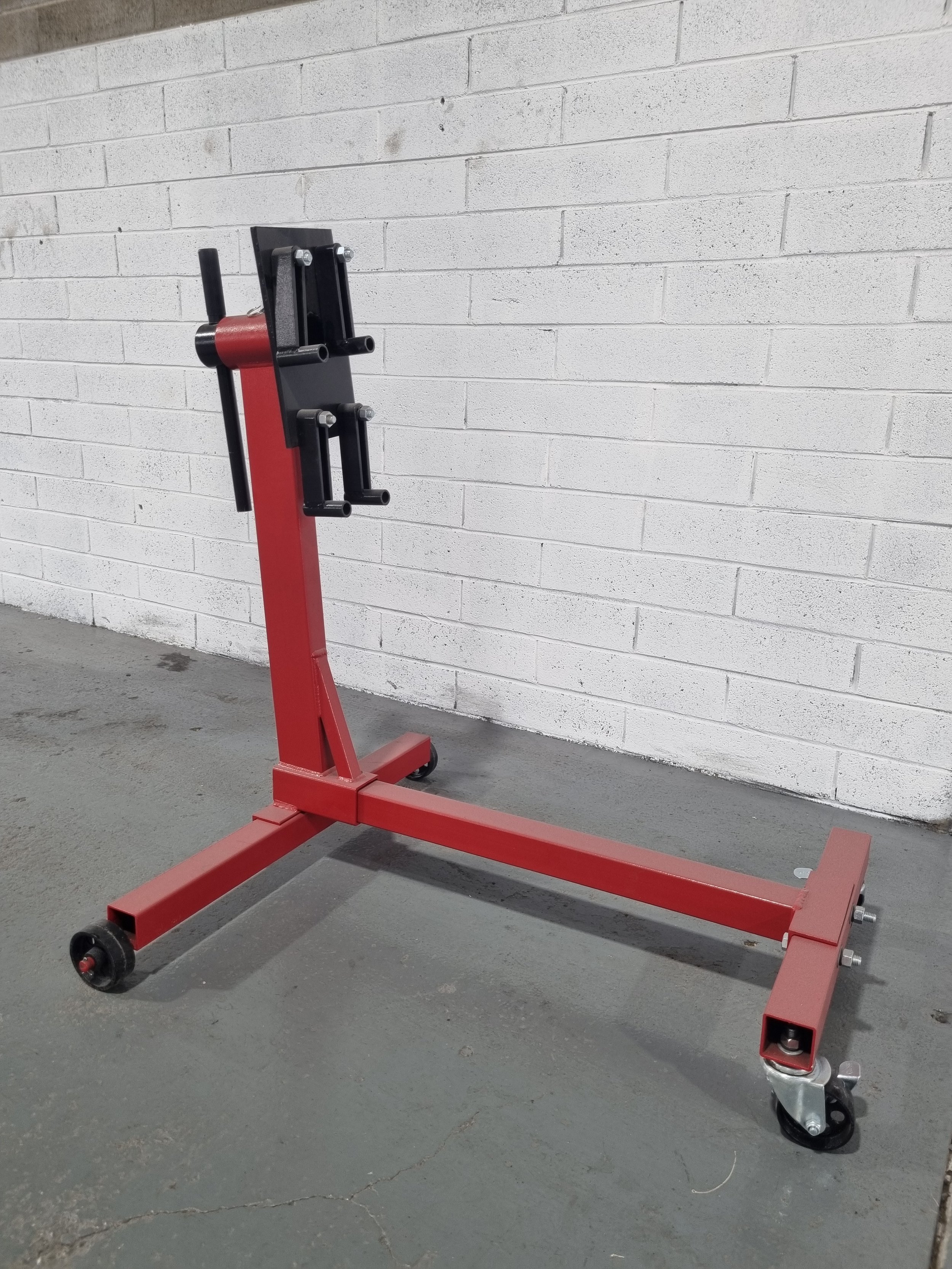 Red adjustable book cart on wheels against a white brick wall.