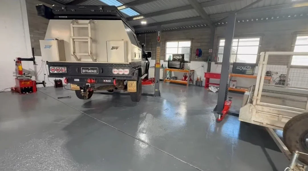 A workshop with a utility truck on a lift inside a garage, equipment and tools organized on shelves and workbenches.