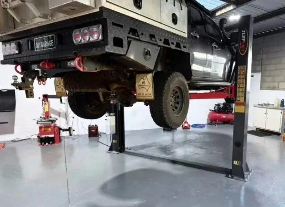 A black off-road vehicle is lifted on a hydraulic car lift in a garage.