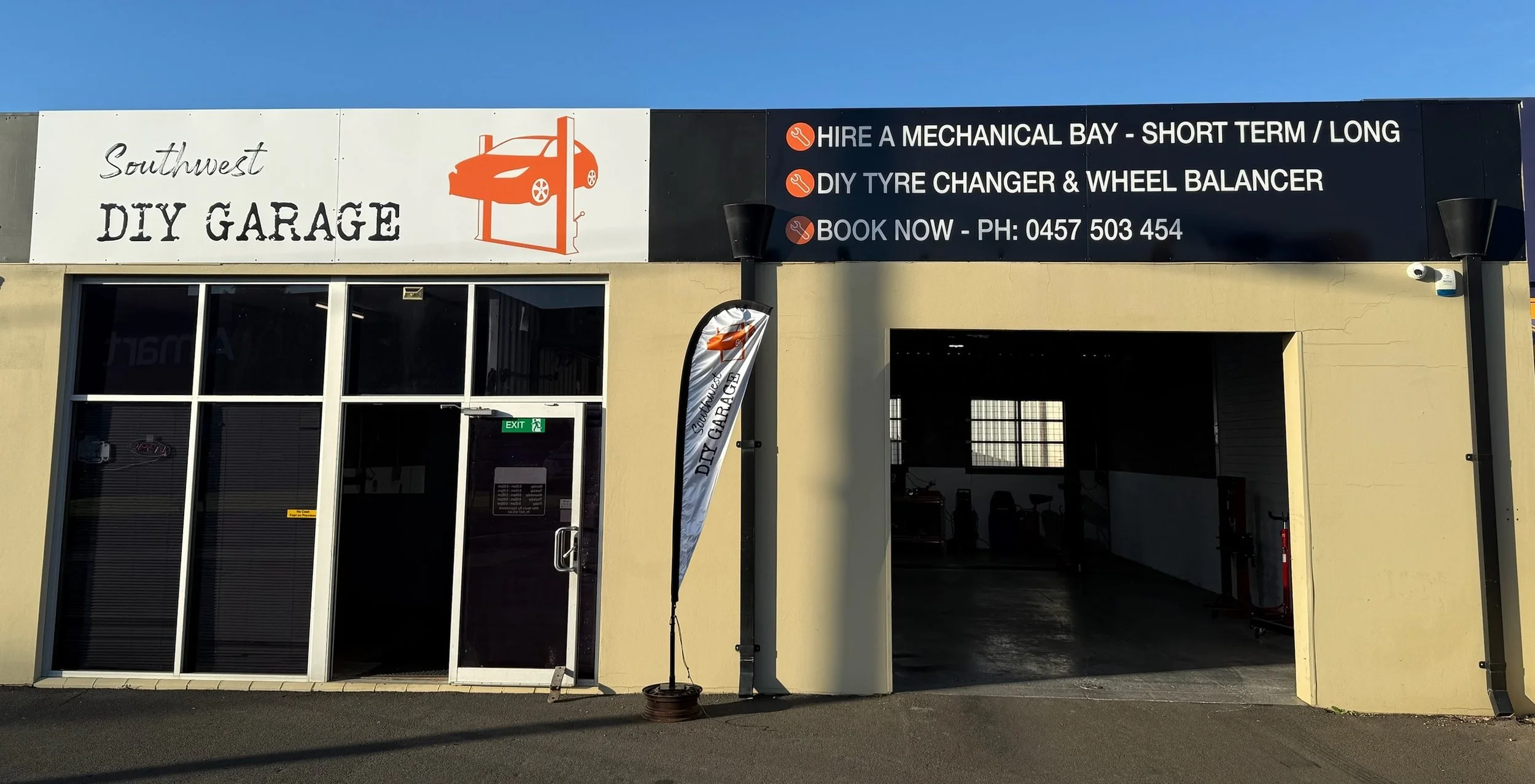 Exterior of a DIY garage with signs advertising mechanical bay rentals and tire services, including the business name 'Southwest DIY Garage' and contact information.