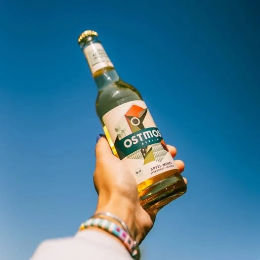 Eine Hand hält eine Flasche Apfel-Minz-Limonade gegen den Himmel. Es ist ein klarer Tag mit blauen Himmel.