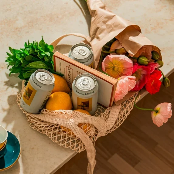 Ein Einkaufskorb mit Getränkedosen, frischen Blumen, einer Zitrone, einem Buch und einem Bündel von Blumen