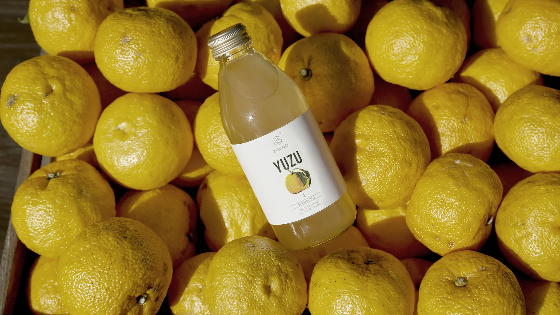 Eine Flasche Yuzu-Sprudel liegt auf einer Ansammlung von gelben Zitronen.