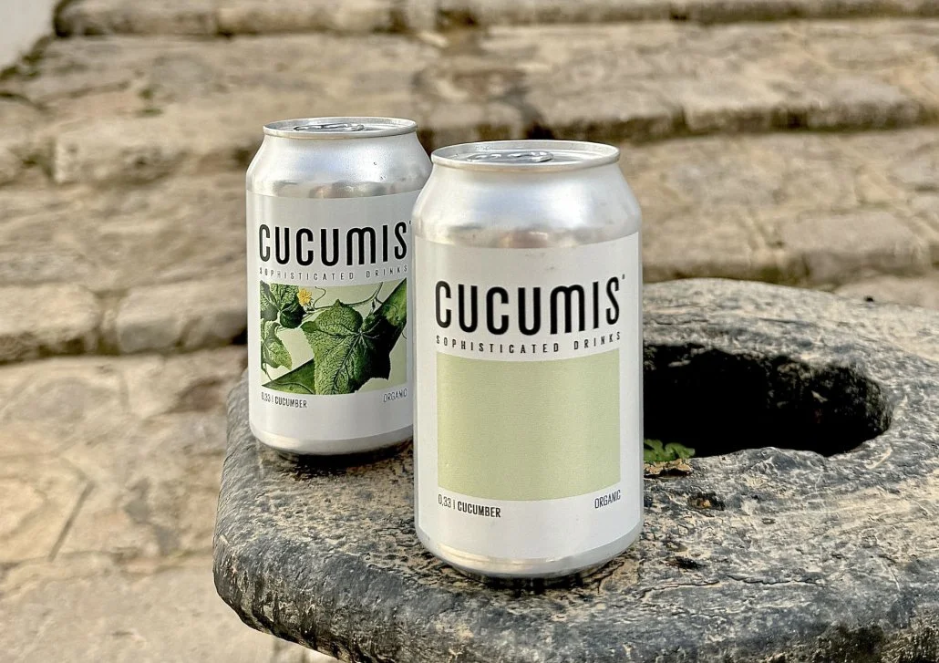 Zwei silberne Getränkedosen mit dem Label "CUCUMIS" auf einem Stein mit einer Höhlung, im Hintergrund eine Steinmauer.