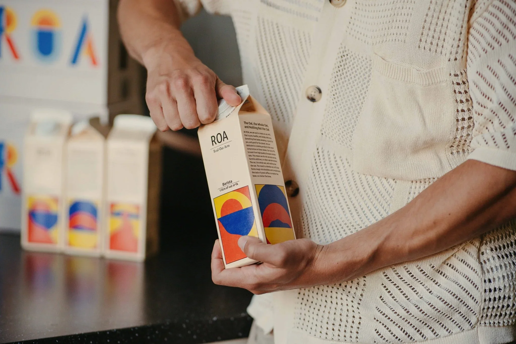 Nahaufnahme einer Person, die eine Tüte mit kunstvollem, farbenfrohem Design hält und darin etwas sieht, während im Hintergrund weitere Tüten mit ähnlichem Design auf einer Oberfläche stehen.