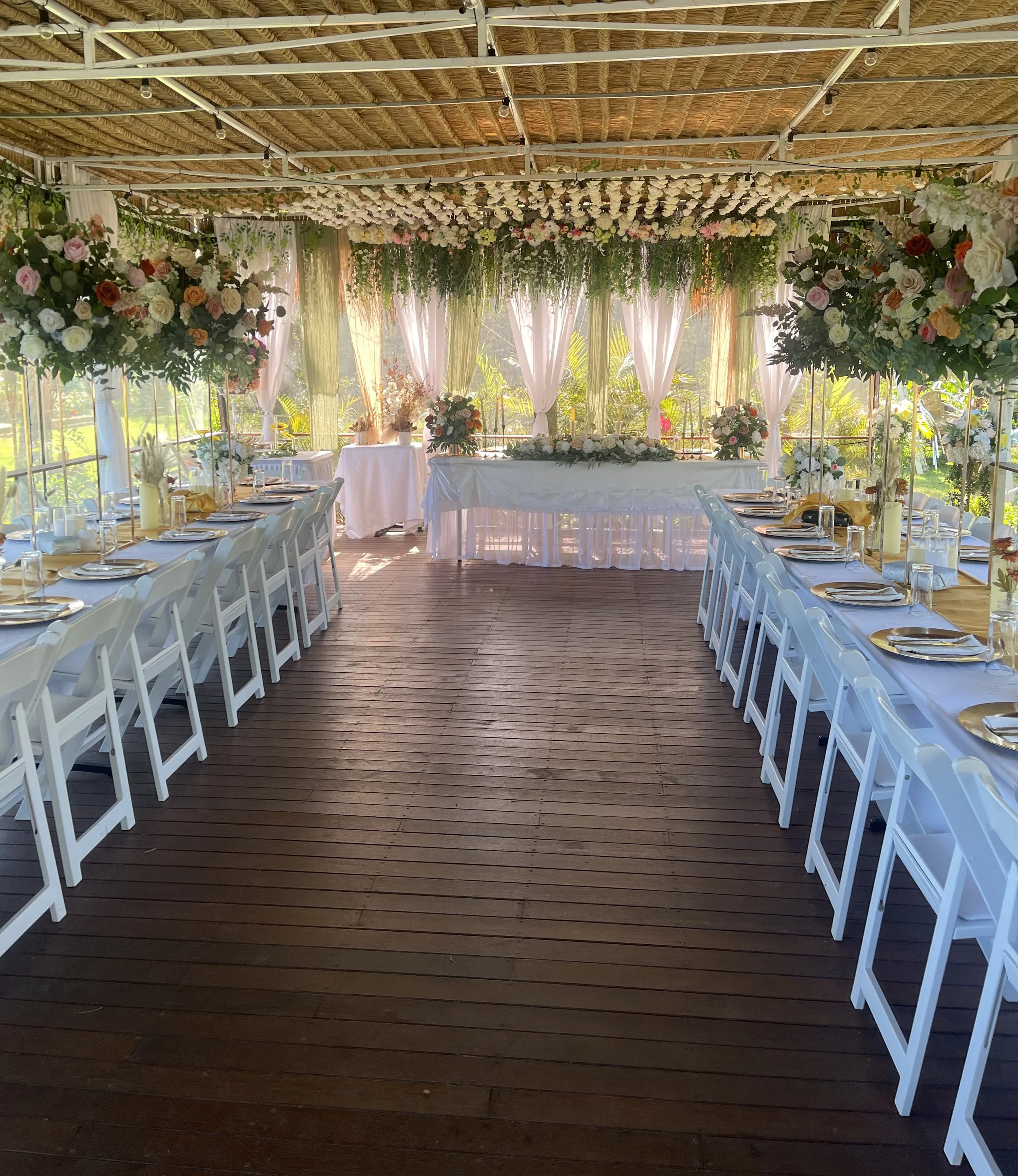 Elegant wedding reception setup with long banquet tables and floral decorations in a bright, airy venue with wooden floors and curtains.