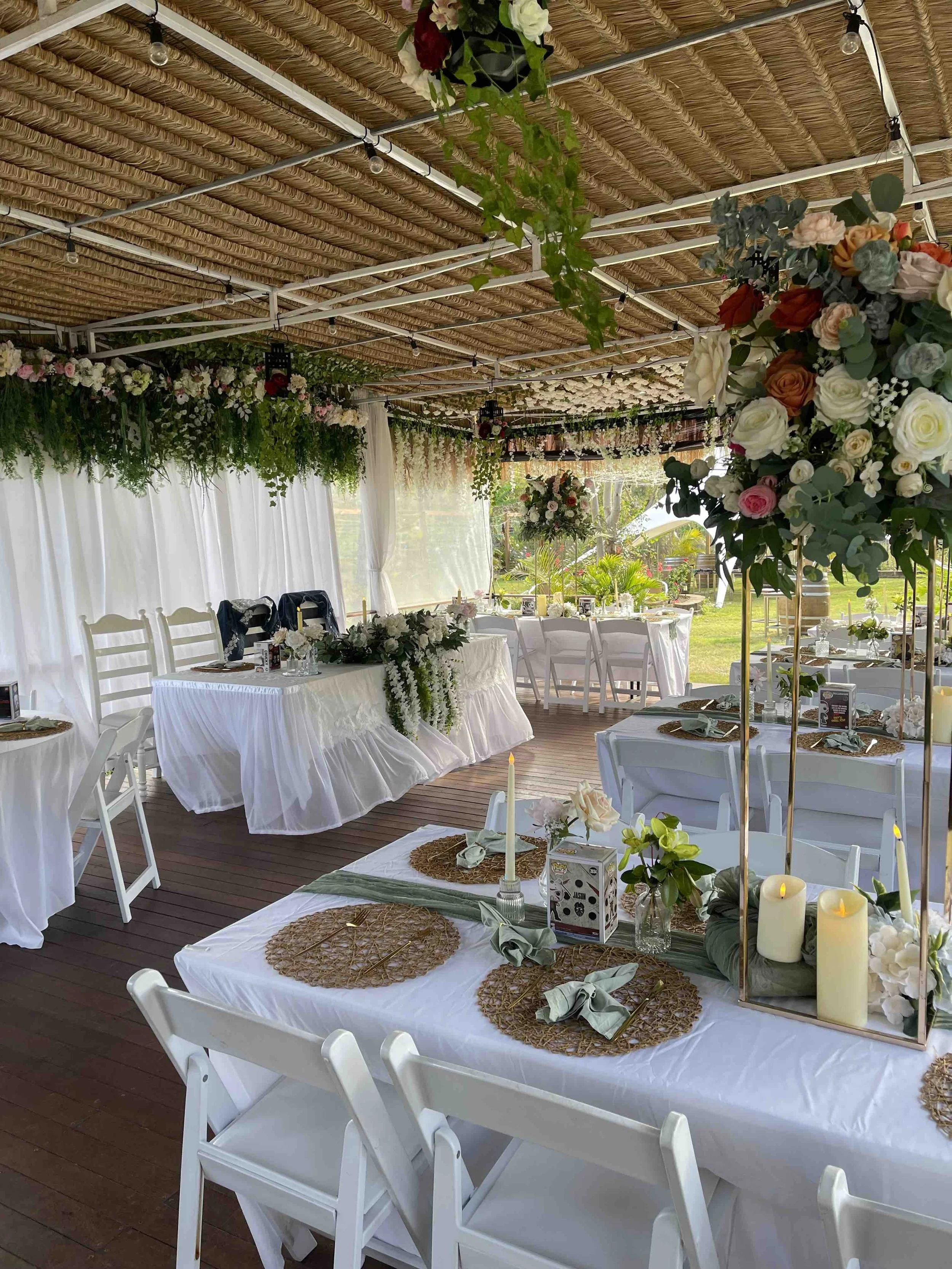 Indoor wedding reception decorated with flowers, candles, and white chairs.
