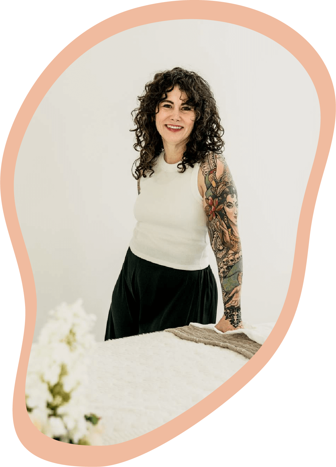 Marhia Ross, massage therapist, smiling while standing beside a massage table in a bright wellness studio.