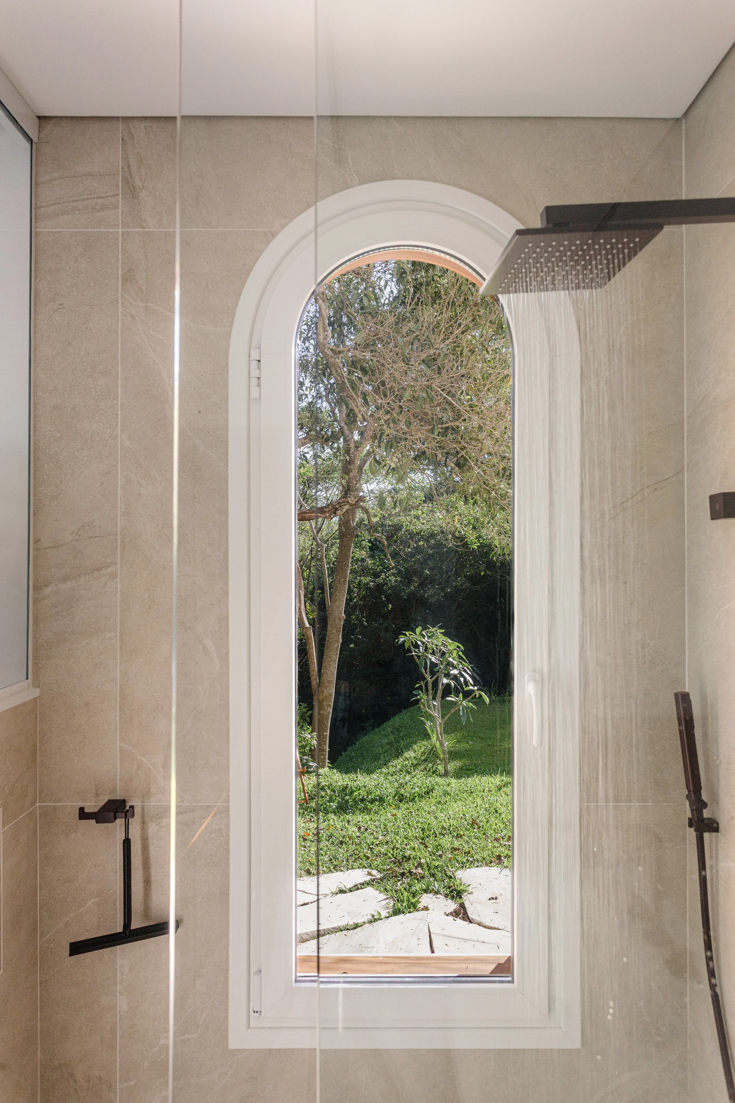 Shower with a large window showing a garden with trees and grass.