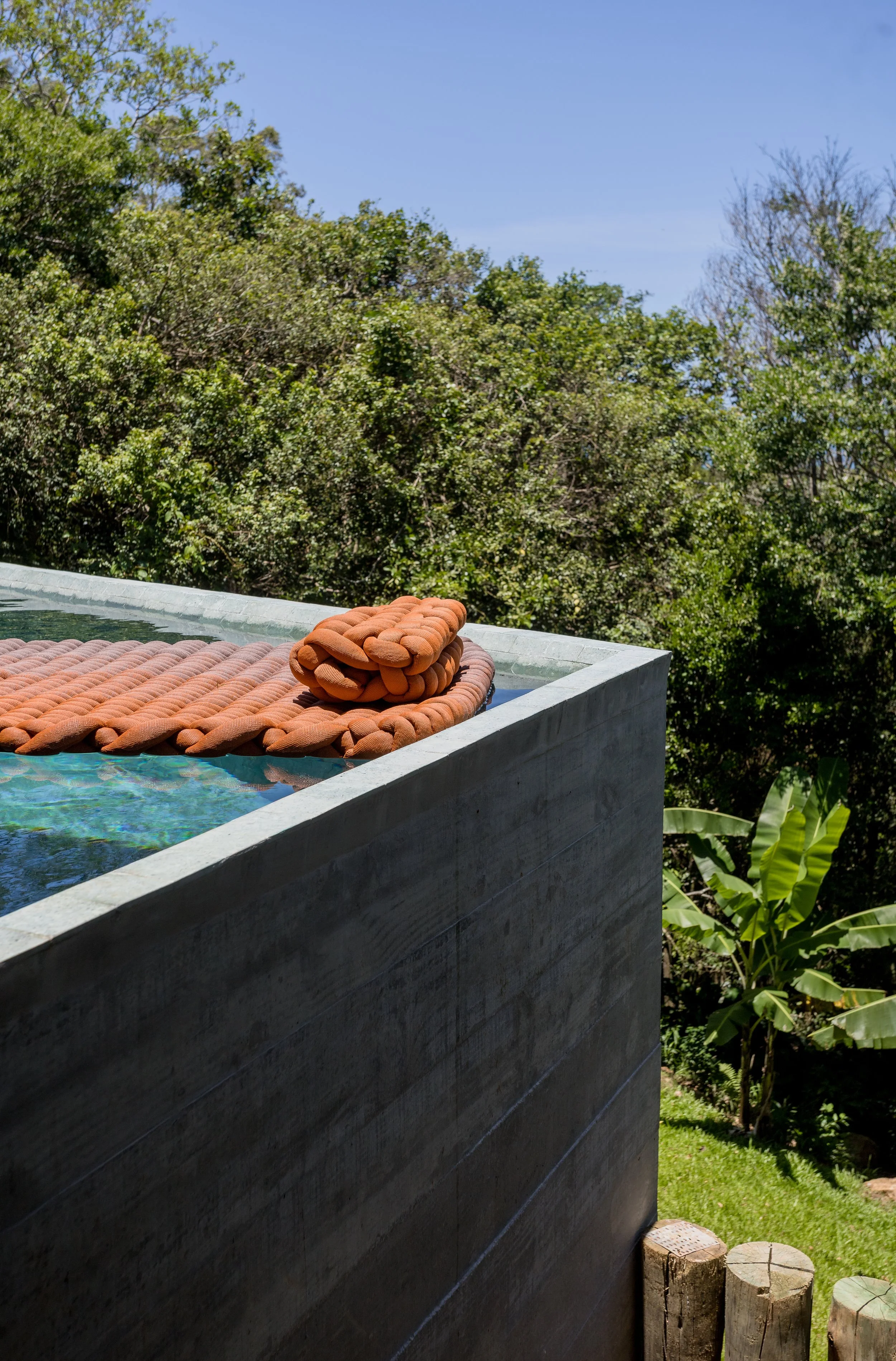 A towel and a pillow on a swimming pool with greenery and trees in the background.