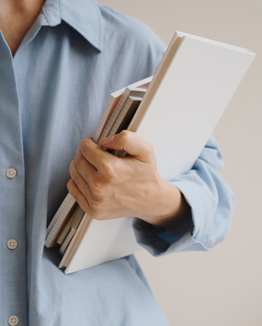 Personne tenant plusieurs livres ou carnets contre sa poitrine, portant une chemise bleue.