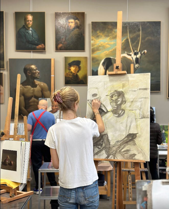 Une élève du cours de dessin à Montreuil dessine un portrait avec du fusain sur toile dans l'atelier d'Edgar Saillen sous une lumière naturelle et inspirante.