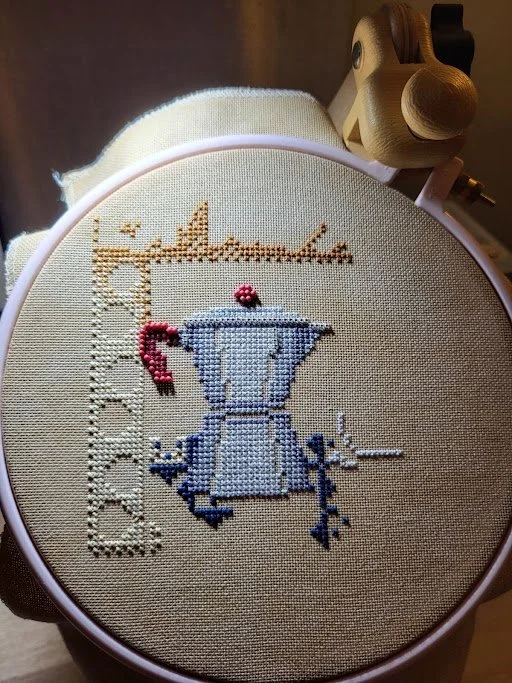 Cross-stitch embroidery of a moka pot with a red handle on beige fabric in an embroidery hoop.  Online cross stitch store.