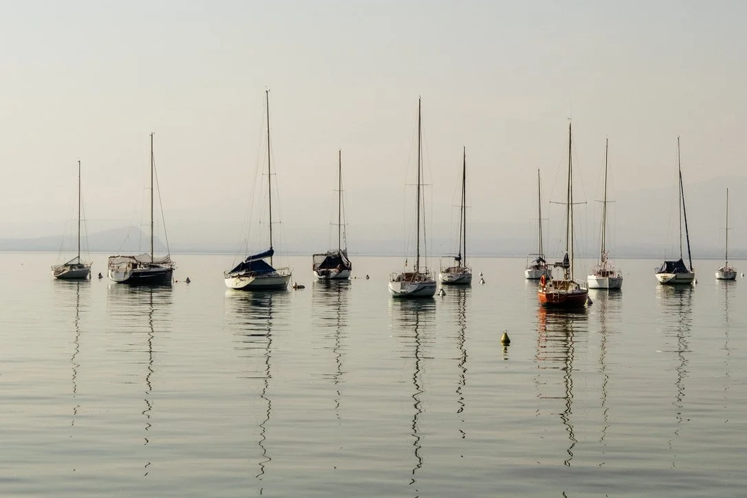 Several sailboats floating calmly on a body of water under a haze sky
