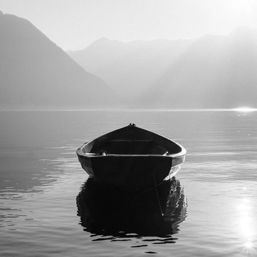 A solitary boat floating on calm water with mountains and a hazy sky in the background.