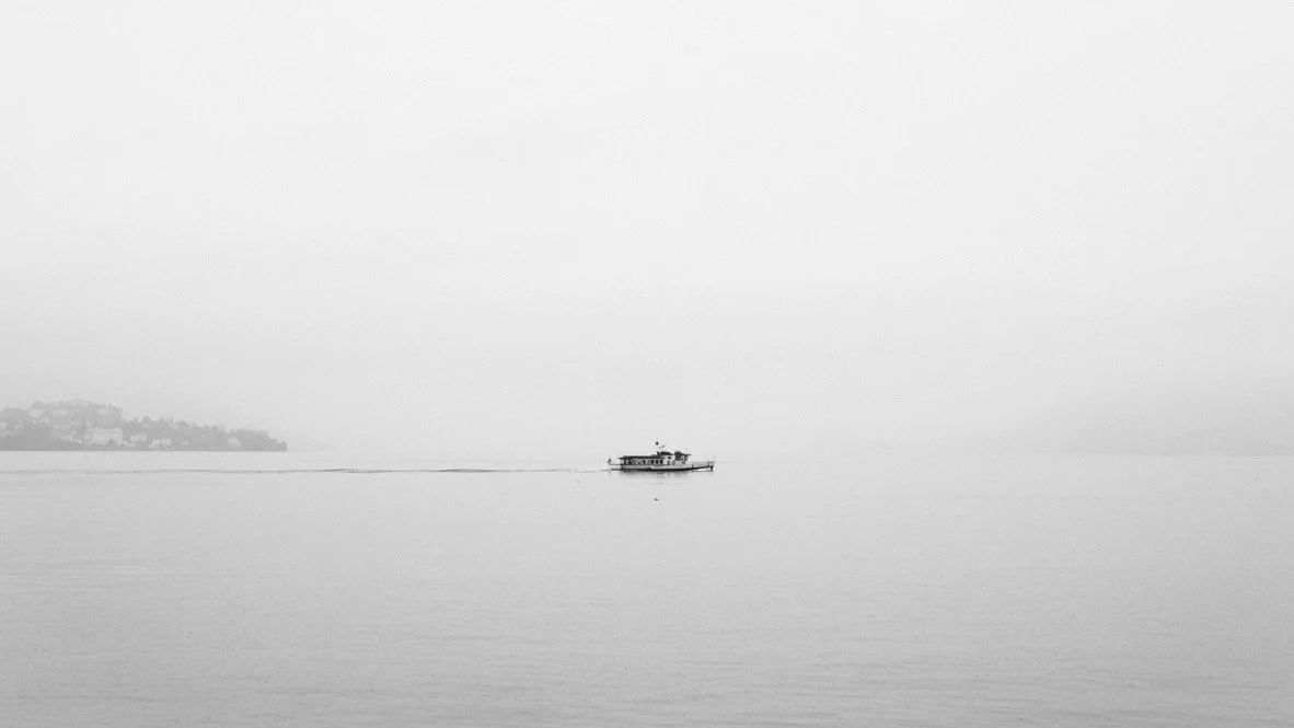 A boat on a calm, foggy body of water with a faint landmass in the distance.