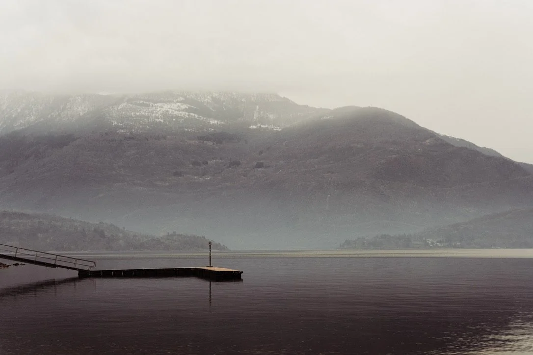 A foggy lake with mountains in the background and a small dock extending into the water.