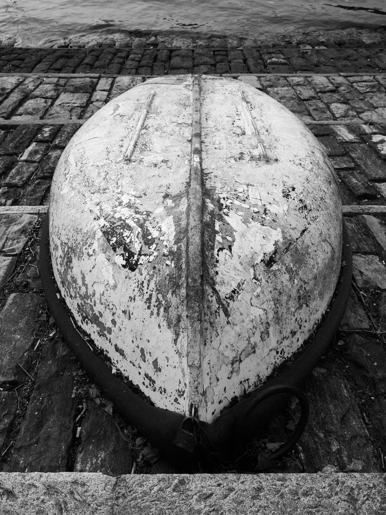 Old, weathered boat with peeling paint resting on a stone dock near water.