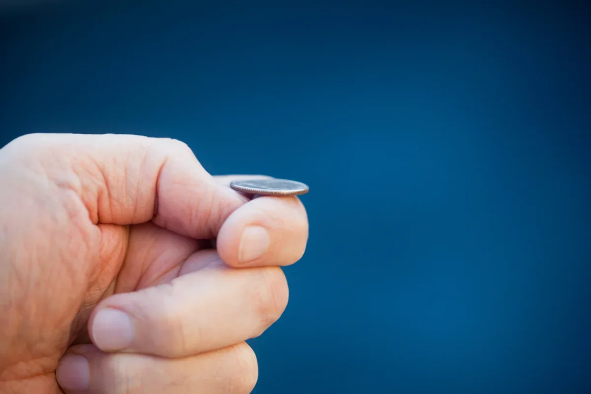 Close-up of a hand holding a coin between thumb and index finger against a dark blue background.
