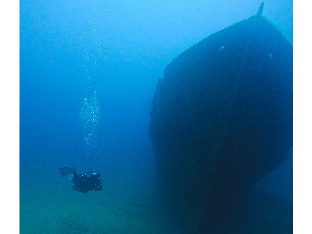 A scuba diver swimming under a sunken shipwreck in the ocean.