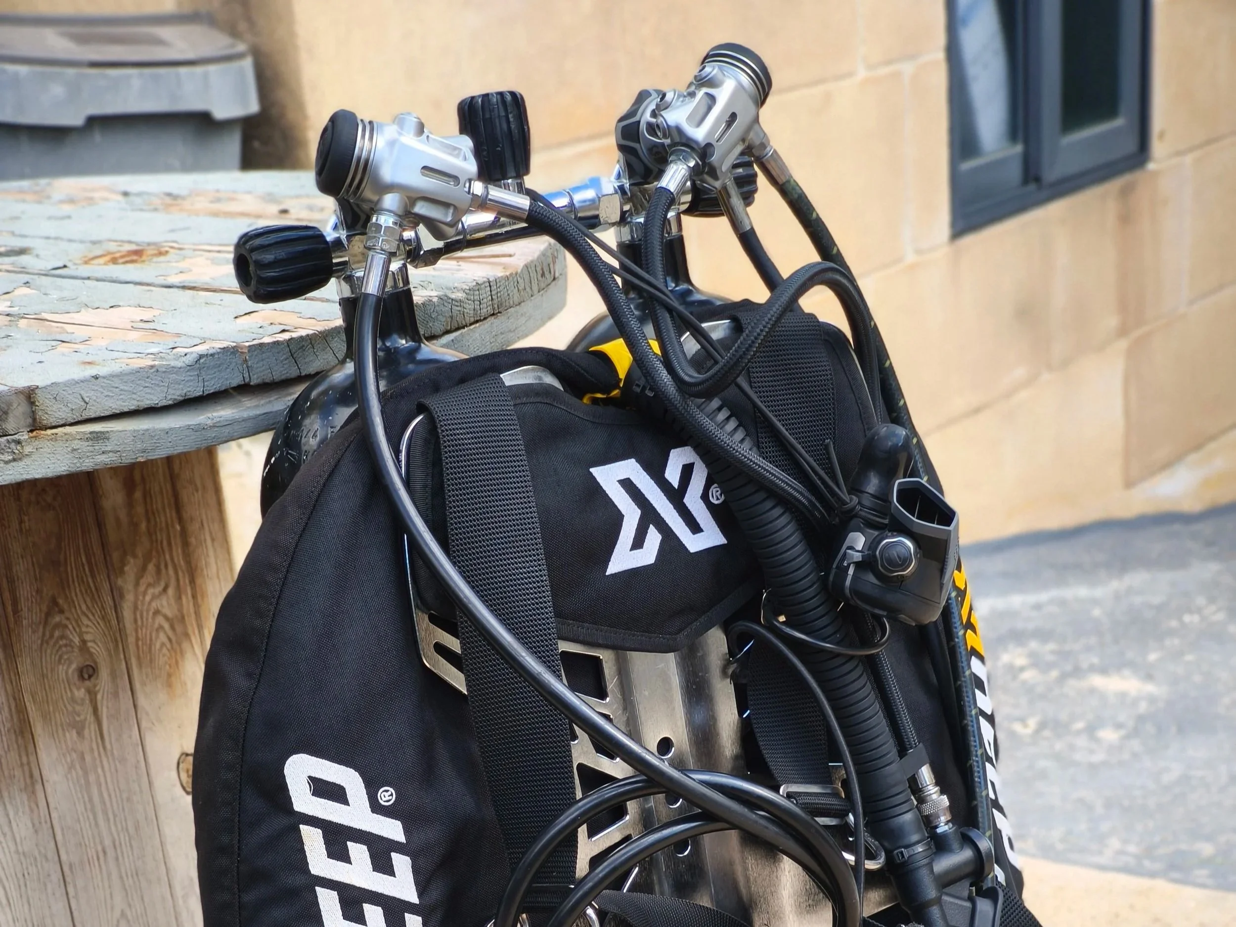 Close-up of a mountain bike leaning against a wooden bench and brick wall, with a black backpack nearby.