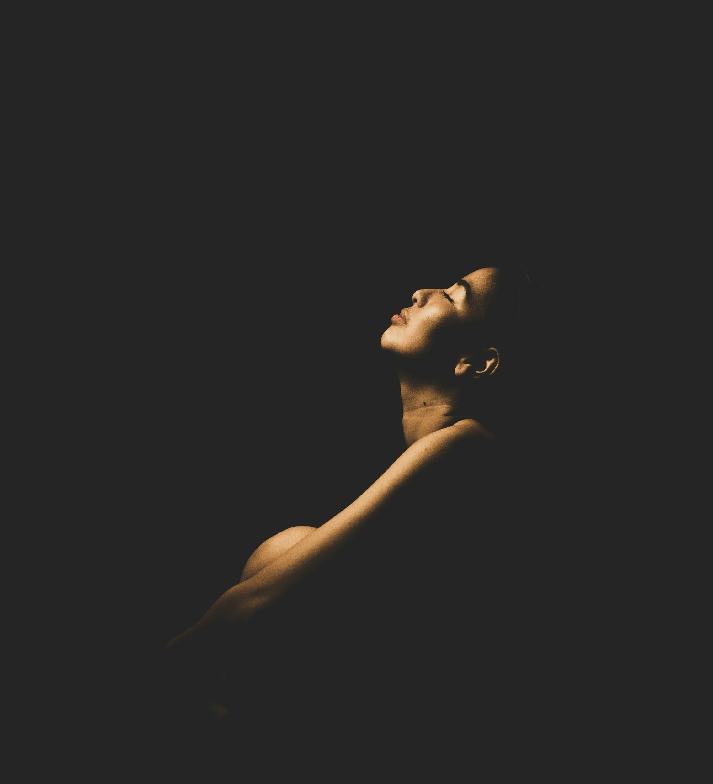 A woman with closed eyes and a serene expression, illuminated softly, against a dark background.