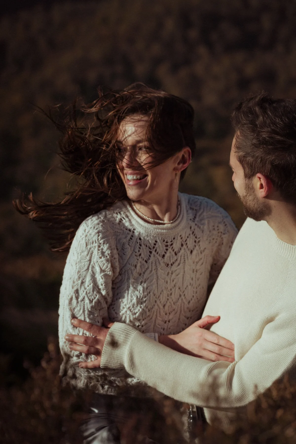A happy couple dancing outdoors at sunset in a grassy field with trees and mountains in the background.