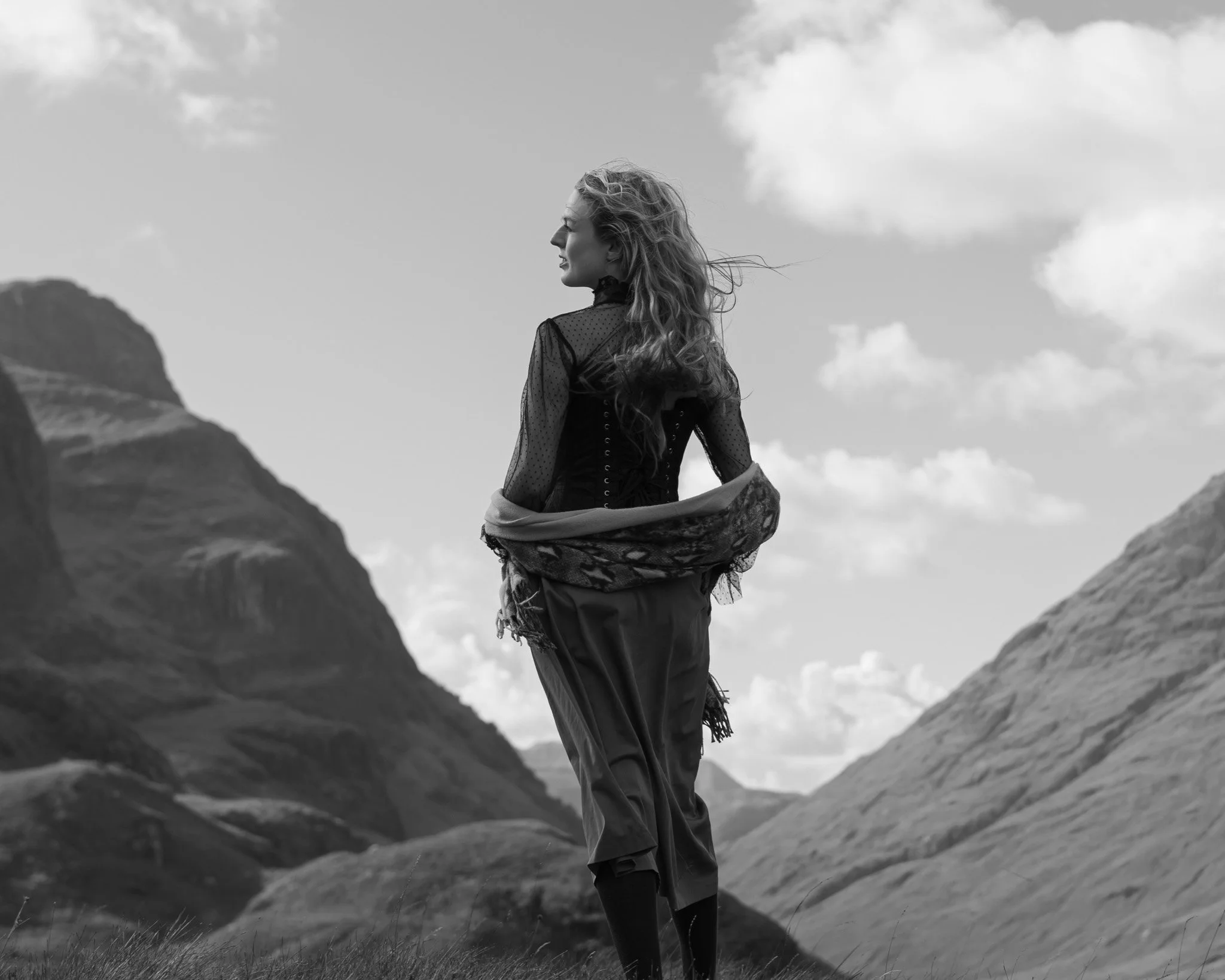 A woman standing outdoors in a mountainous landscape with clouds in the sky, dressed in vintage clothing and salvador Dali inspired
