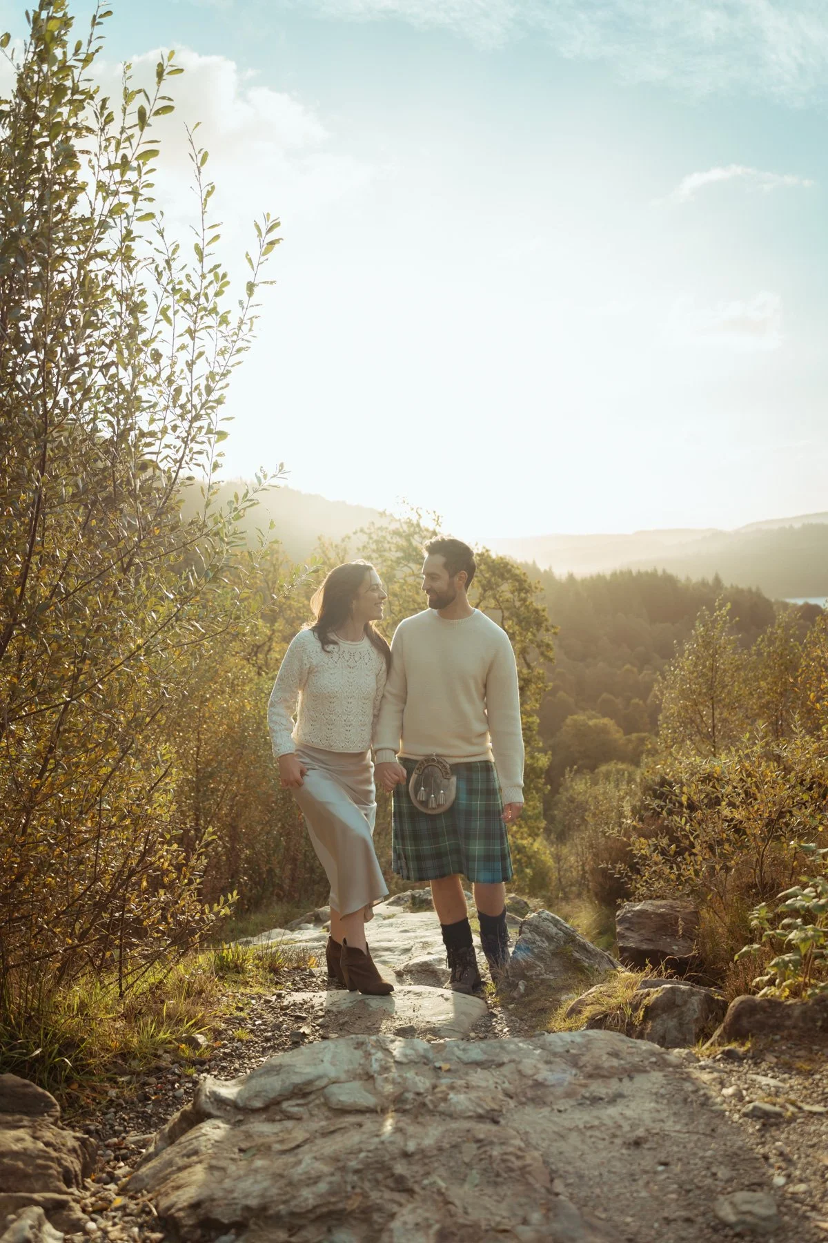 A romantic couple climb stone steps lit by the blazing sunrise, surrounded by autumnal trees