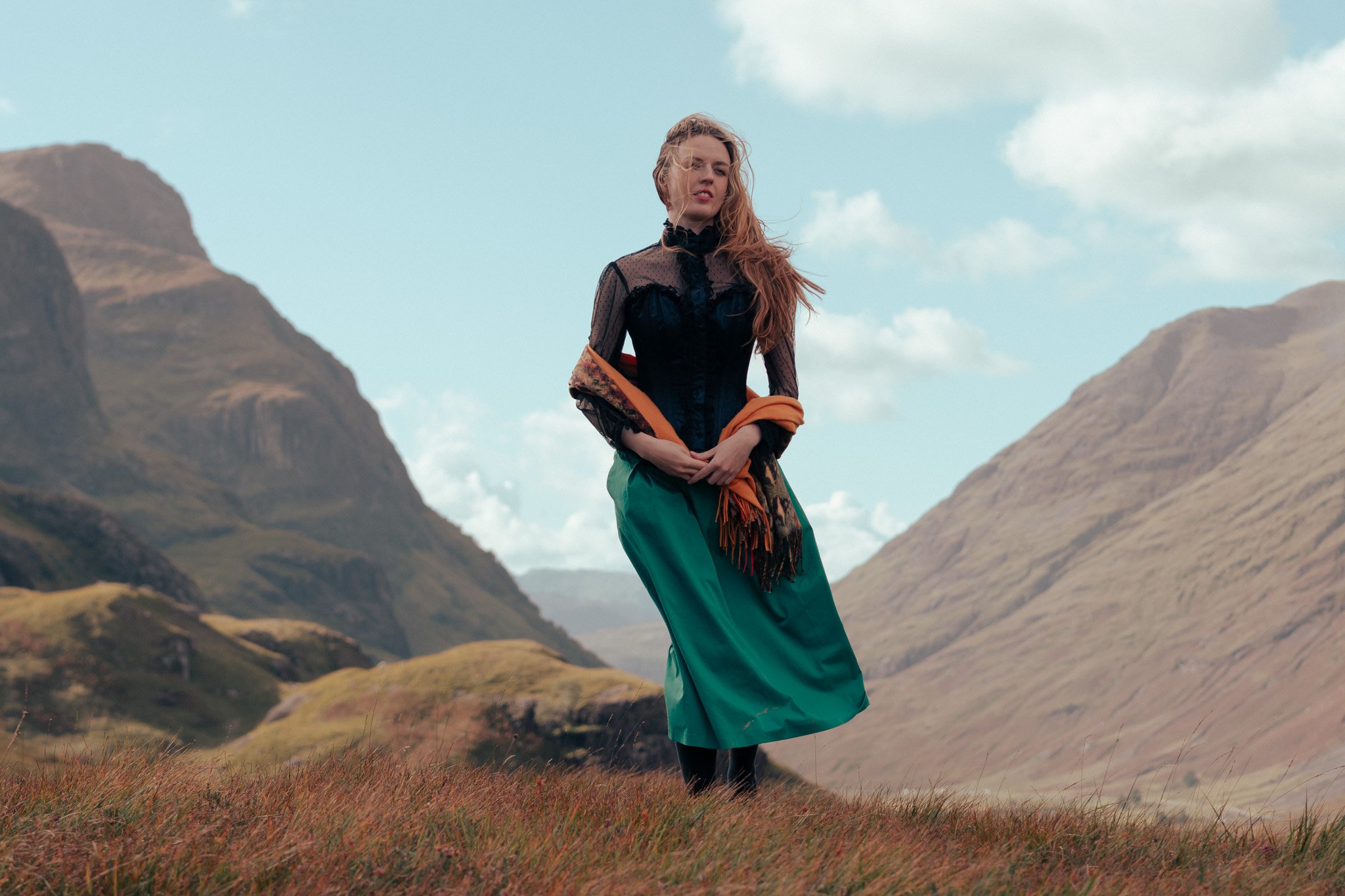 A woman standing in a grassy field with mountains and cloudy sky in the background, from the sound of music