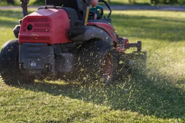 A red riding lawn mower cutting grass in a backyard.
