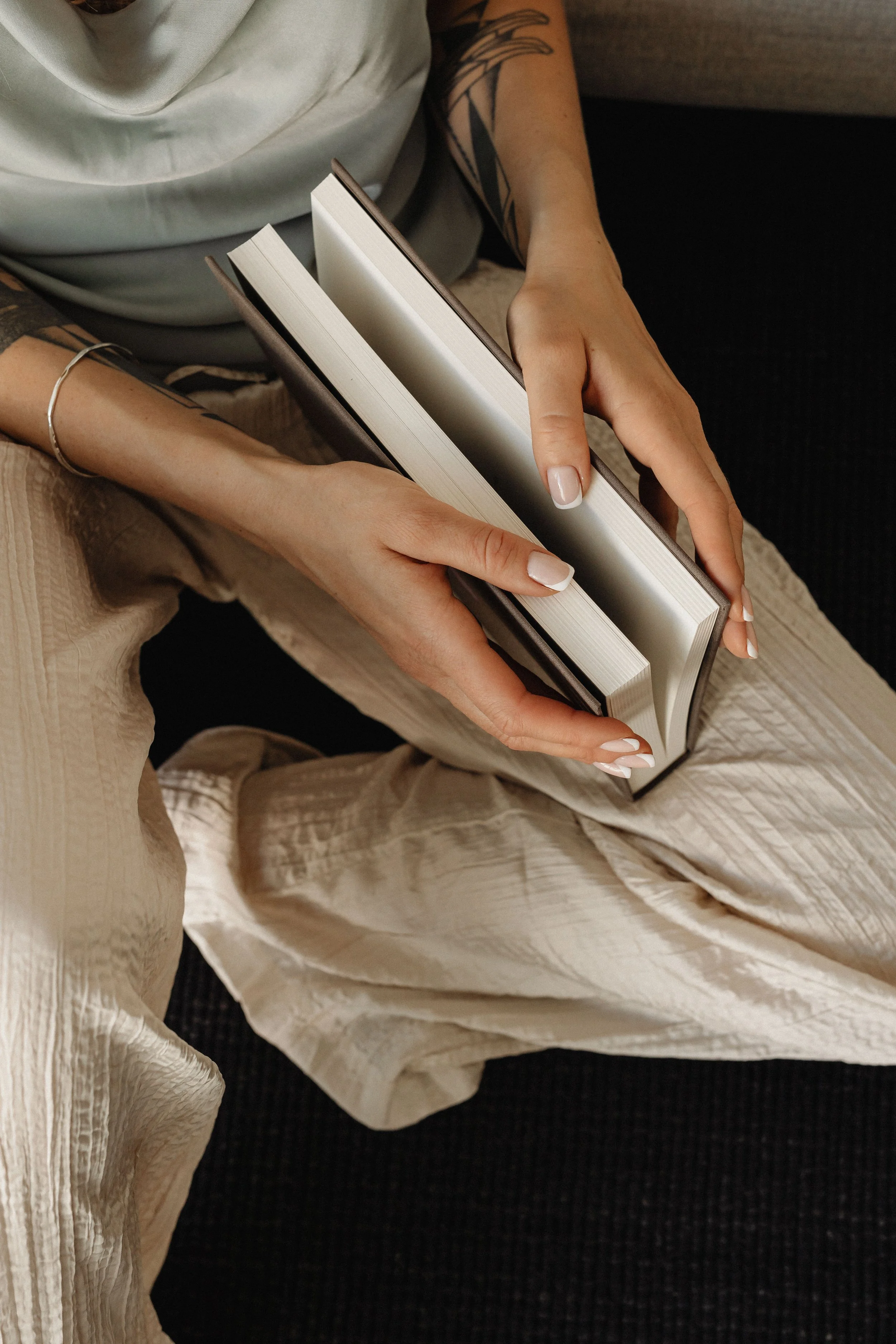 Person holding an open book with blank pages, seated on a sofa.